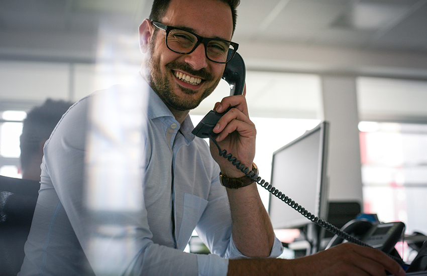 man happily working at a desk and answering the phone